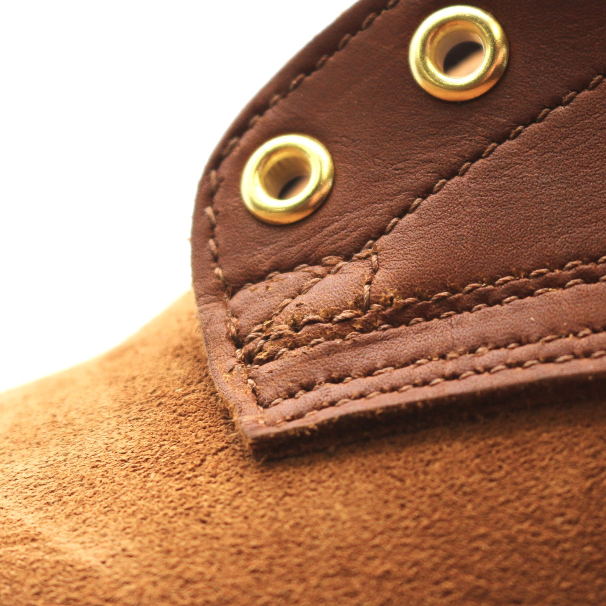 Close-up detail of a brown leather strap with brass grommets and a textured brown suede or suede-like surface below, photographed on a white background.