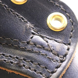 Close-up of a dark navy leather item featuring detailed black stitching and shiny brass grommets.
