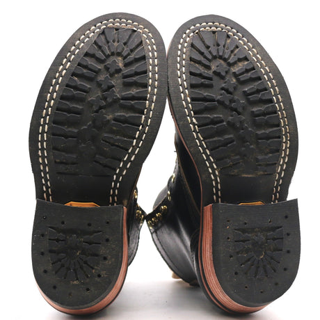 The soles of a pair of black leather boots, showing the treaded black rubber outsoles with white stitching, a black heel cap with a starburst pattern, and a tan leather midsole.