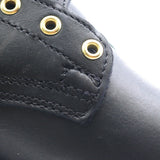 Close-up detail of a black leather boot showing the side panel, stitching, and brass eyelets against a white background.