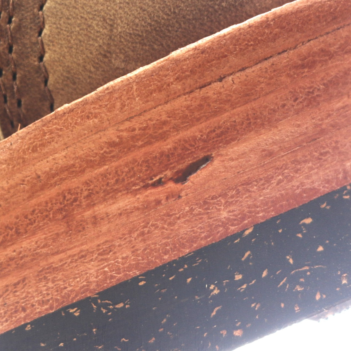 Close-up detail of a brown leather or wood trim piece with visible grain texture, a small dark defect, and a black speckled surface below.