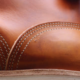 Close-up of a warm tan leather item with white contrast stitching and a small visible scratch or scuff on the surface.