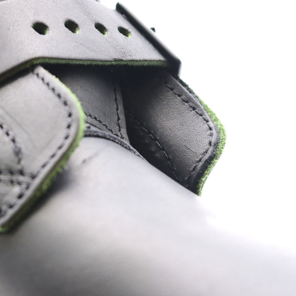 Close-up detail of a gray leather strap or buckle closure with visible green edging and stitching on a white background.