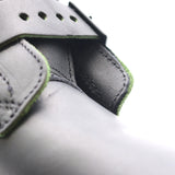 Close-up detail of a gray leather strap or buckle closure with visible green edging and stitching on a white background.