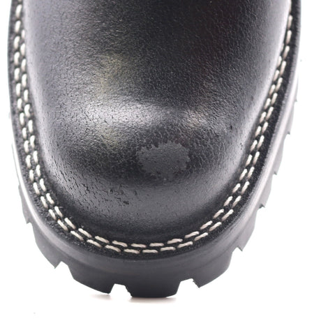 Close-up of a black leather boot toe showing white contrast stitching and a black treaded sole on a white background.