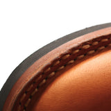 Close-up detail of a leather shoe or boot corner showing a warm tan leather upper, stitched edge, and a dark outsole against a white background.