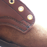 Close-up detail of a brown leather shoe or boot showing a stitched overlay panel with brass grommets and a suede-like brown footbed.