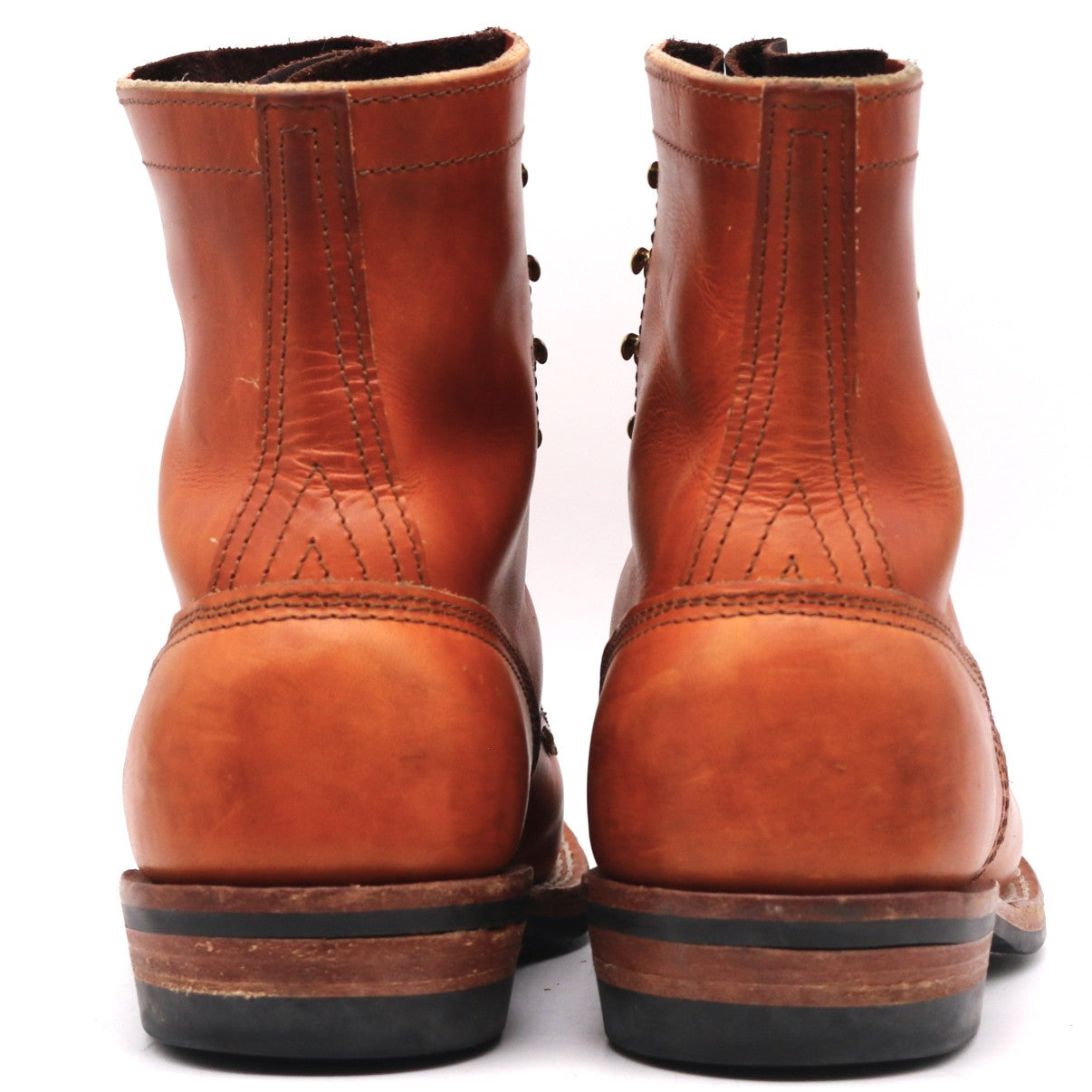 A pair of classic redwing-style leather ankle boots shown from the back, featuring a warm cognac brown leather upper with decorative stitching and a black and brown stacked sole.