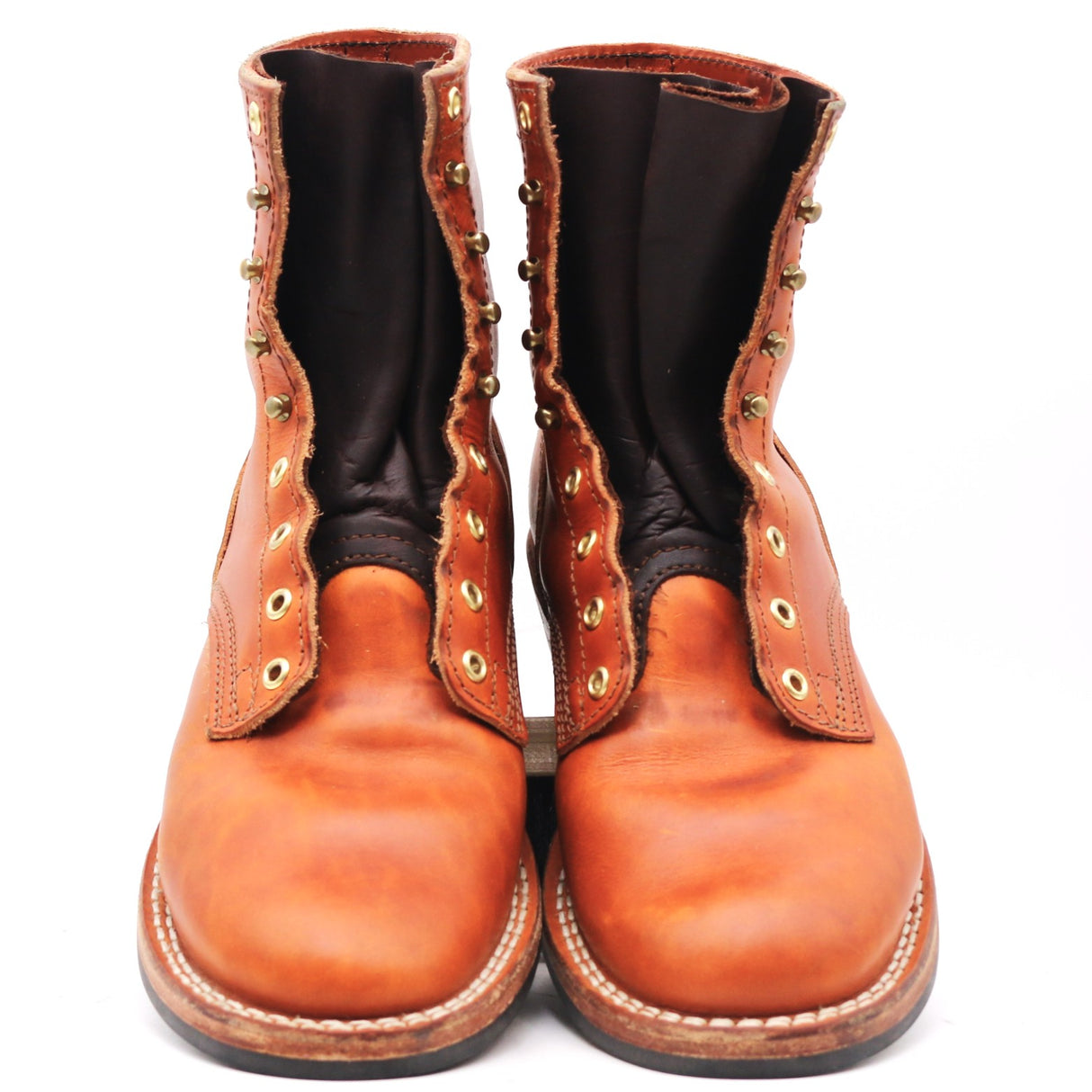 A pair of men's tall brown leather boots with decorative brass grommets and studs, shown from the front against a white background.