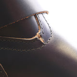 Close-up of a dark brown leather boot showing a stitched leather detail with the edge of the leather slightly worn and exposed.
