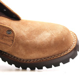 Close-up of a tan suede work boot showing the toe cap, stitching, metal eyelet, and dark rugged sole on a white background.