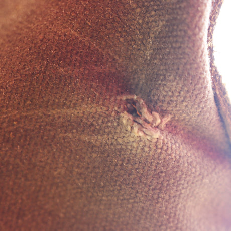 A close-up shot of a textured brown leather or faux-leather surface with a small, distressed tear or scuff near the center.