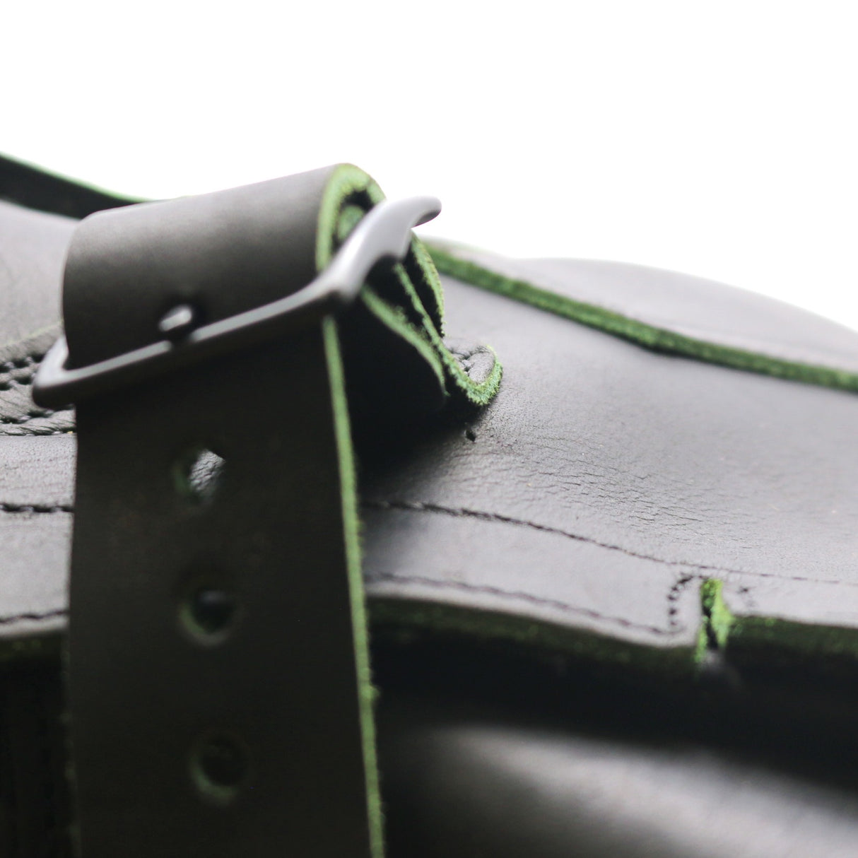 Close up photo of an exposed sewing hole underneath the strap and buckle of a black tanker boot.