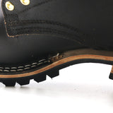 Close-up of a black leather lace-up boot showing the side profile, including brass eyelets, stitching, a tan midsole, and a black lug sole on a white background.