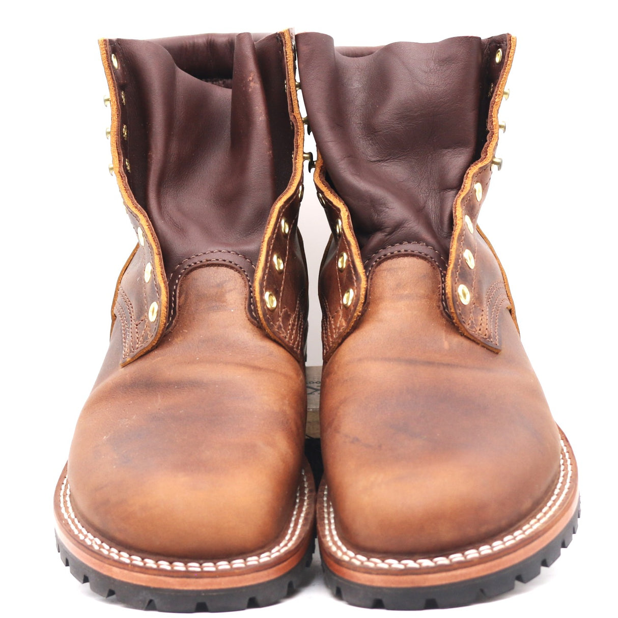 Pair of brown leather boots with brass hardware shown from the front at a slightly elevated height in front of a white background. Boots show signs of wear.