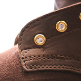 Close-up detail of a brown suede or nubuck boot showing a stitched collar with gold-tone metal grommets on a white background.