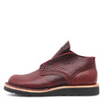 A single men's ankle boot in textured burgundy leather with a pebbled grain, featuring a black sole and a thin tan midsole layer, shown from a side profile on a white background.