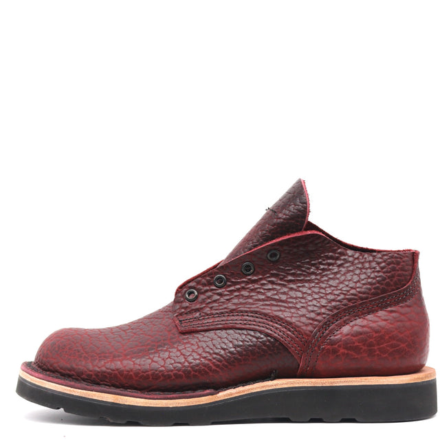 A single men's ankle boot in textured burgundy leather with a pebbled grain, featuring a black sole and a thin tan midsole layer, shown from a side profile on a white background.