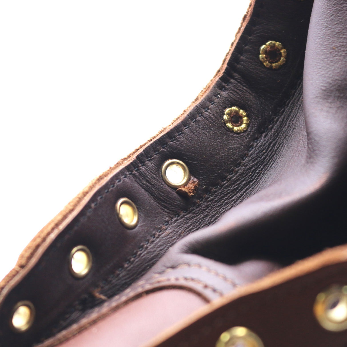Close up photo of the gusset and eyelets of a brown boot. The fourth eyelet from the bottom has a cut in the leather underneath it.