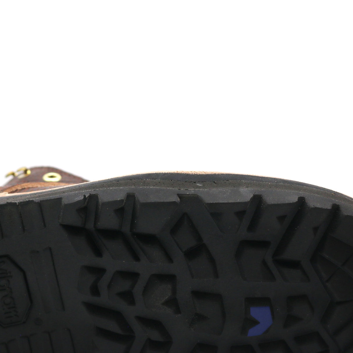 Close-up of the treaded black rubber sole of a brown boot, showing a small blue chevron logo and a gold grommet on a white background.