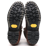 A pair of boots shown from the sole view, featuring a black Vibram treaded outsole with a distinctive yellow Vibram logo on the heel and white contrast stitching along the edge.