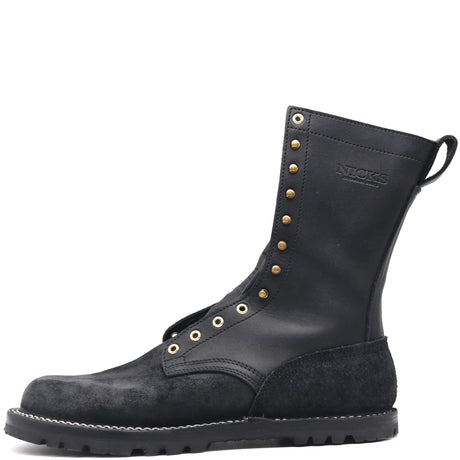 A black leather and suede mid-calf work boot with brass eyelets and studs, featuring a pull tab and the brand name 'NICKS' embossed on the side, set against a plain white background.