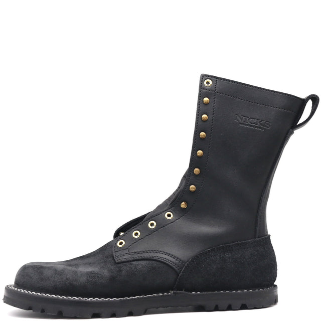 A black leather and suede mid-calf work boot with brass eyelets and studs, featuring a pull tab and the brand name 'NICKS' embossed on the side, set against a plain white background.