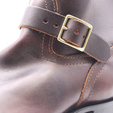 Close-up of a dark brown leather boot strap with a gold-tone metal buckle, showing detailed stitching and texture.