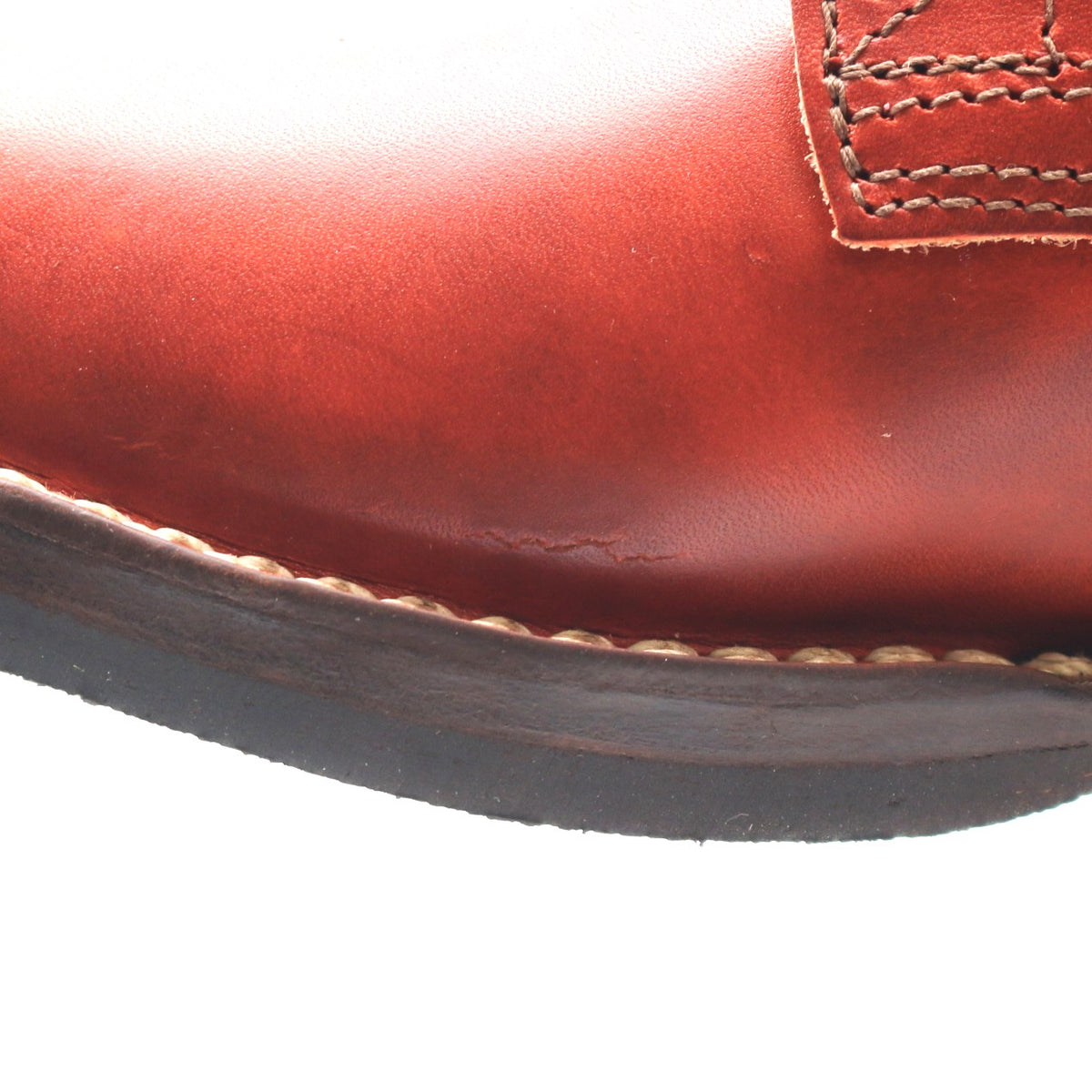 Close-up of a reddish-brown leather boot showing the toe, stitching, and a portion of the dark sole against a white background.