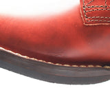 Close-up of a reddish-brown leather boot showing the toe, stitching, and a portion of the dark sole against a white background.