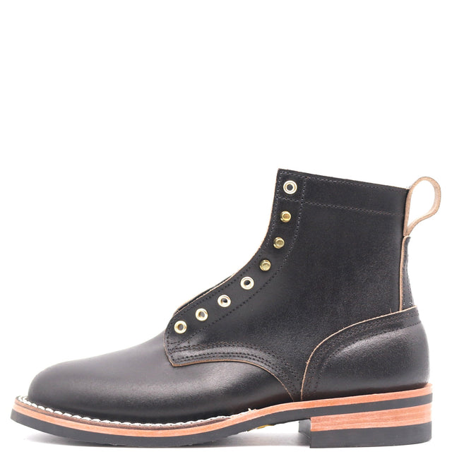 A black leather ankle boot with gold-tone metal eyelets, contrast stitching, and a stacked black sole with a tan outsole, shown from a side profile on a white background.