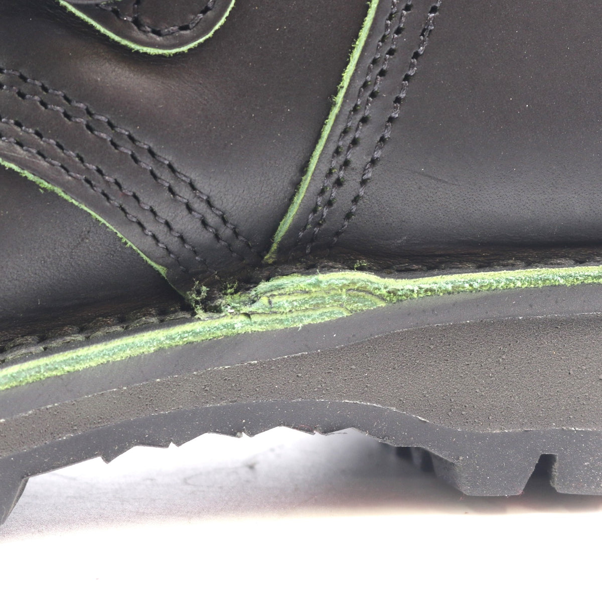 Close-up of a black leather boot showing a heavily worn, frayed, and damaged green sole edge.