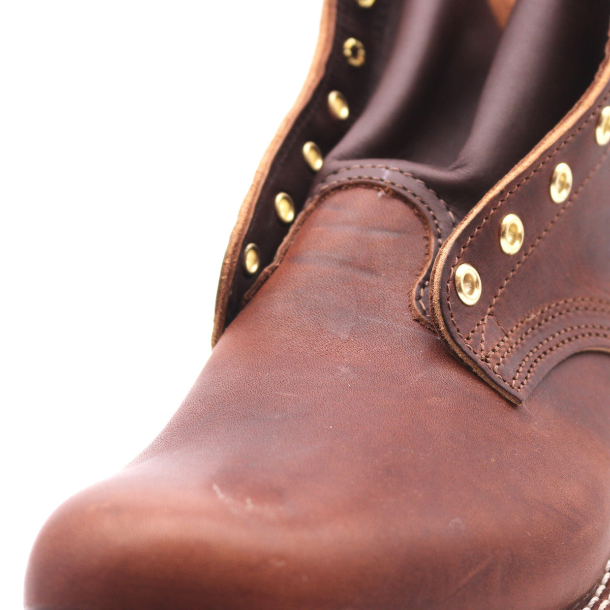 Close up of the front instep of a brown leather boot showing visible scrapes, scratches, dings, and dents.