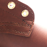 Close-up detail of a brown leather strap or holster with double stitching and two brass grommets on a white background.