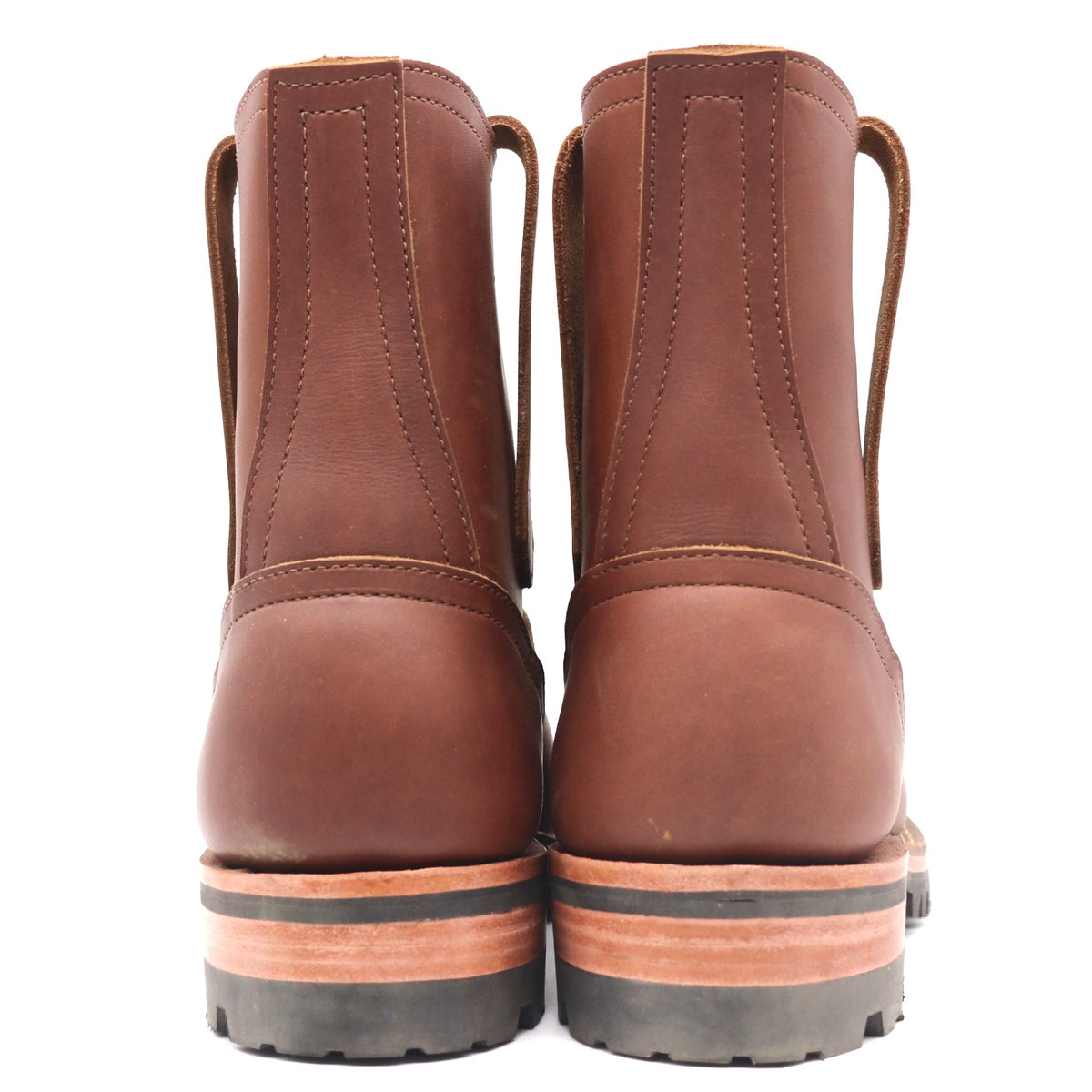 A pair of brown leather lace-up ankle boots shown from the back, featuring stacked rubber soles with a black tread and a tan mid-layer, set against a plain white background.