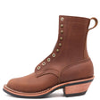 A brown leather lace-up ankle boot with brass eyelets, a pull tab, and a stacked wood-look heel, shown from a side profile on a white background. The brand 'NICK'S' is embossed on the side.