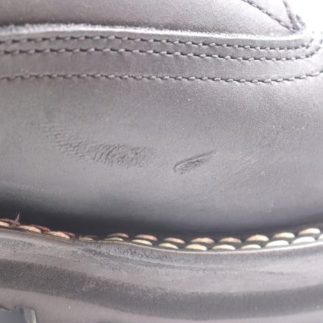 Close-up of a dark gray leather shoe upper with visible scuffing and scratches on the side, showing stitching details.
