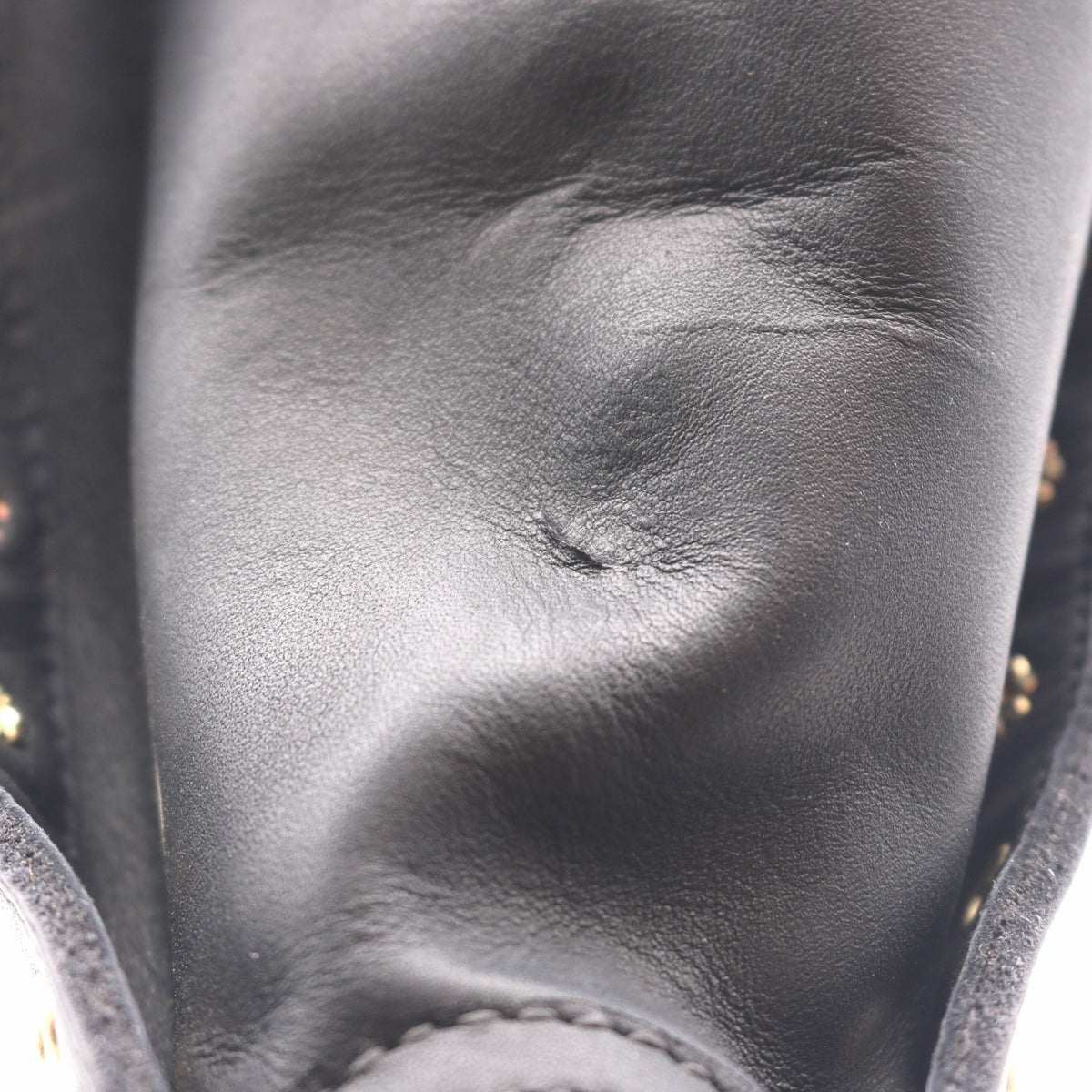 Close-up of a black leather boot or shoe showing the textured leather surface, stitching, and small gold-tone studs along the side.