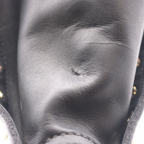 Close-up of a black leather boot or shoe showing the textured leather surface, stitching, and small gold-tone studs along the side.