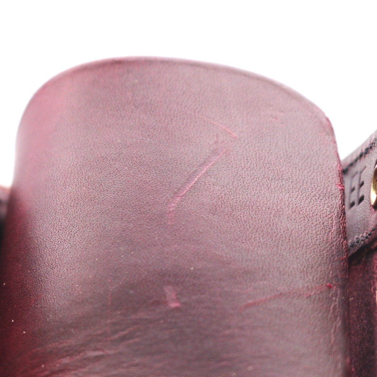 Close-up of a dark burgundy leather strap or belt section showing the textured leather surface and stitching against a white background.