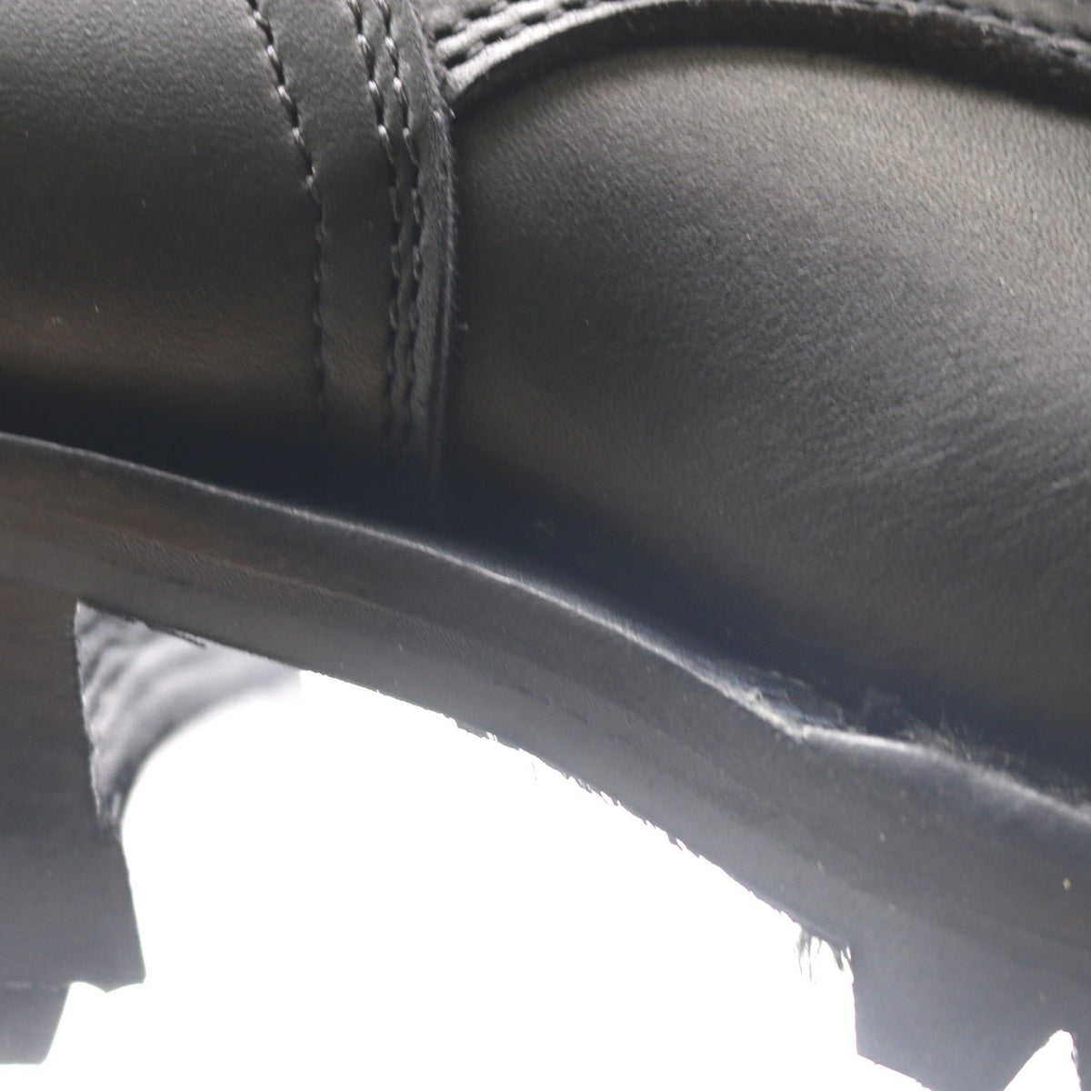 Close-up detail of a black leather boot showing the side panel, stitching, and a portion of the sole.