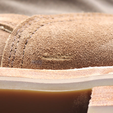 Close-up detail of a brown suede shoe upper with visible stitching and a thick tan outsole.