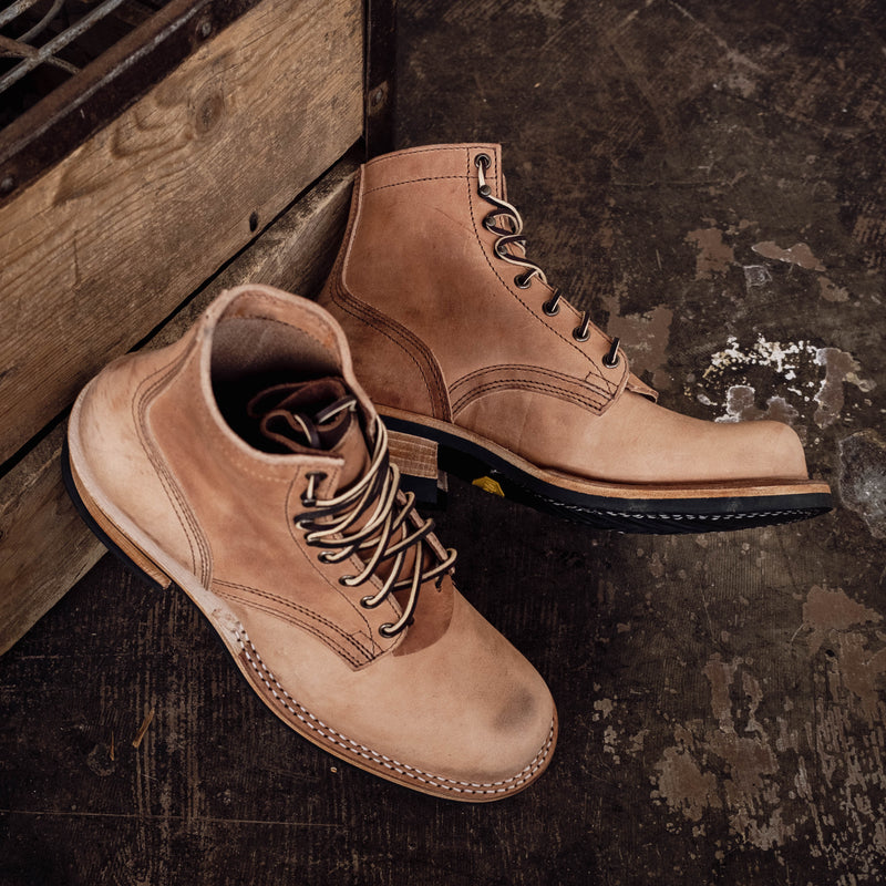 Pair of tan leather work boots with dark laces heavy stitching and thick lug soles leaning against a wooden crate