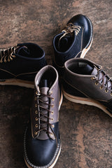 Pair of black leather boots with brown soles on a textured surface