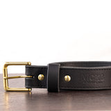 Black belt with brown stitching and brass hardware sitting on metal surface