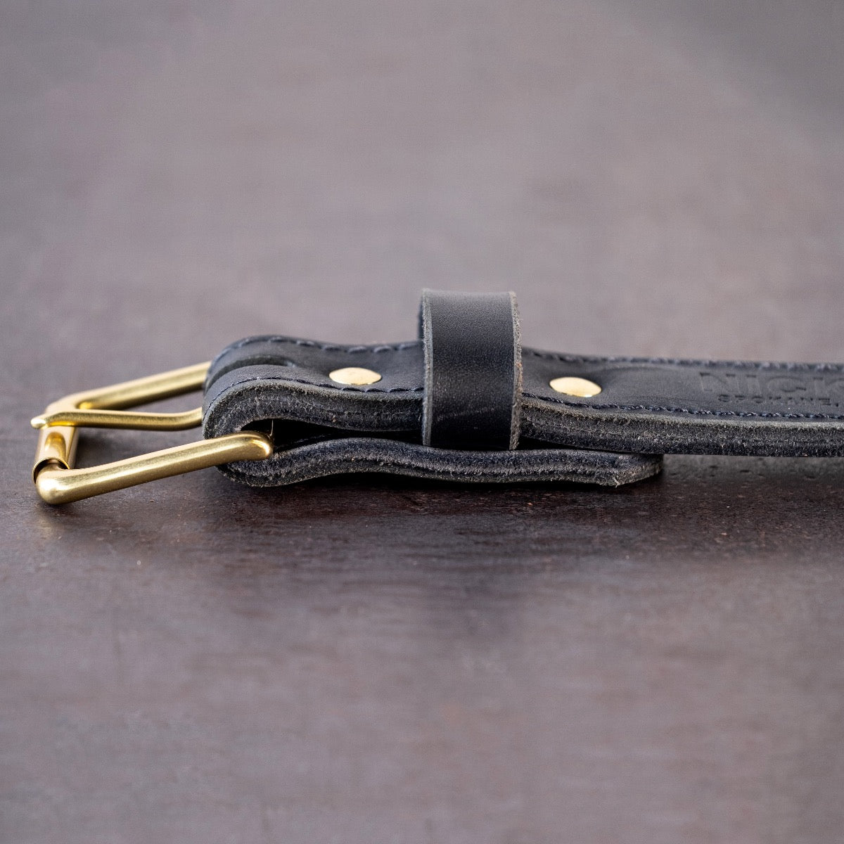 Black belt with brown stitching and brass hardware sitting on metal surface