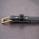 Black belt with brown stitching and brass hardware sitting on metal surface