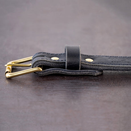 Black belt with brown stitching and brass hardware sitting on metal surface