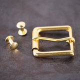 Brass belt buckle and brass Chicago screws sitting on a metal surface