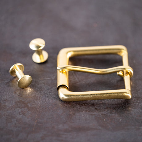 Brass belt buckle and brass Chicago screws sitting on a metal surface